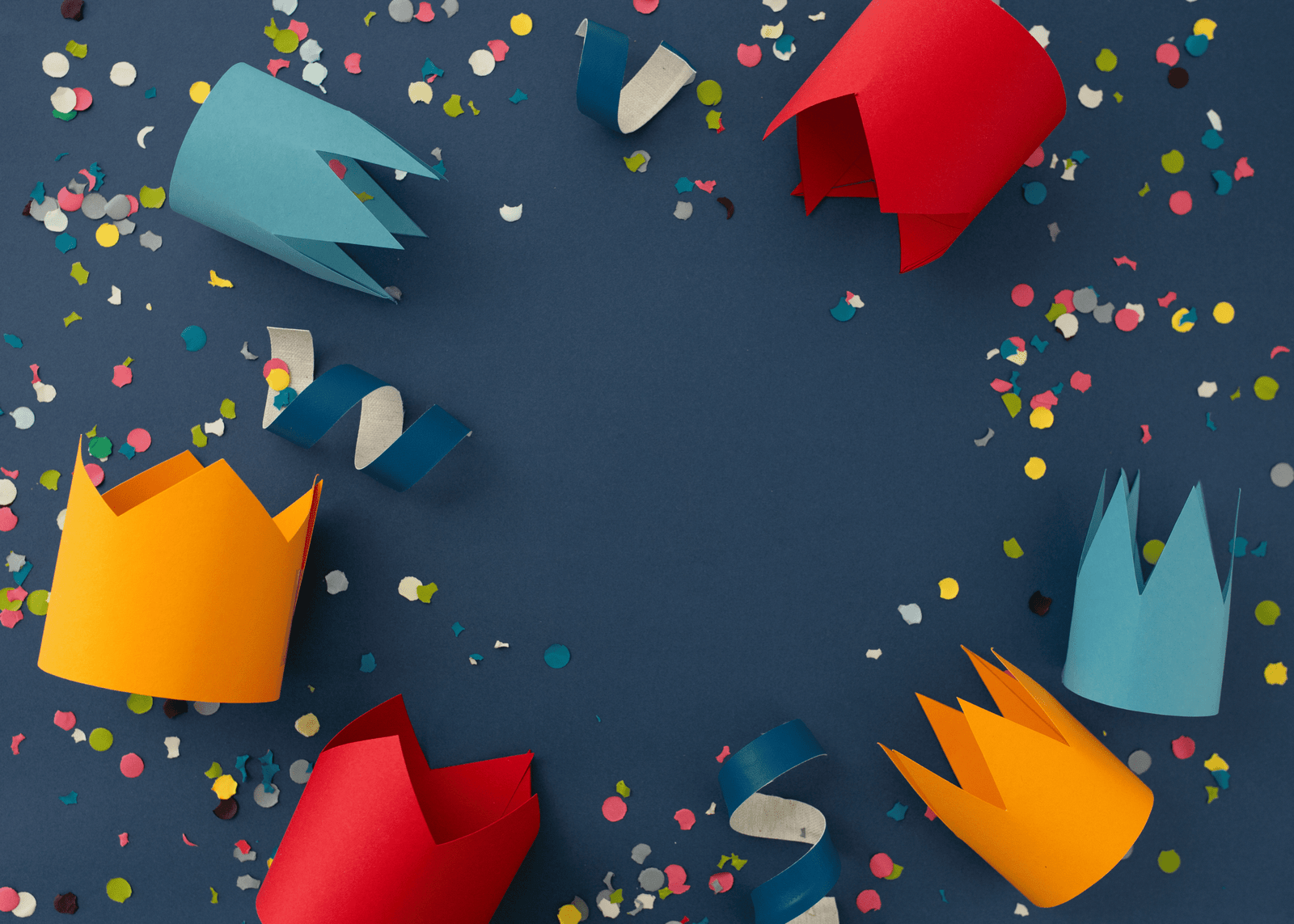 Coronas de papel de colores, serpentinas y confeti sobre fondo azul, ideales como manualidades fáciles para decorar fiestas en casa.